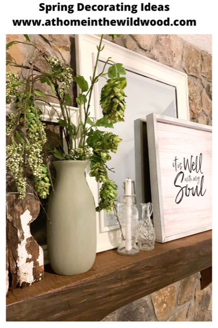 A cottage style mantel decorated for spring with faux greenery, a mirror, a picture, and empty frames