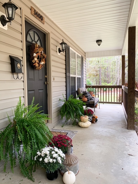 A front porch decorated for fall showcasing a black front door painted with fusion mineral paint