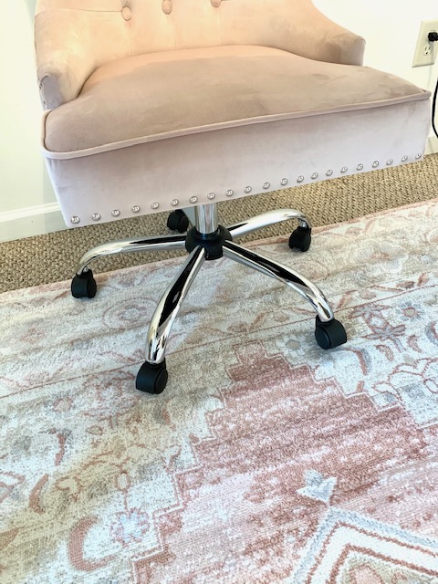 A blush colored office chair sits on an equally beautiful blush colored area rug