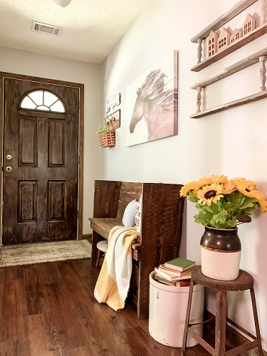 a front foyer is decorated for a early fall with sunflowers, a vintage pew, and art work