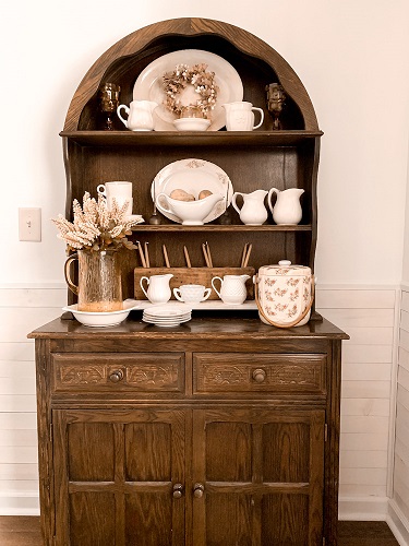 A vintage hutch in a dining room decorated with ironstone and other thrifted finds