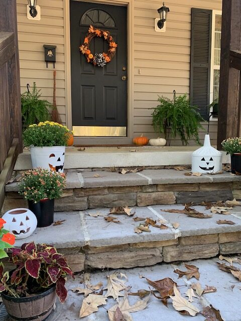 Cottage front porch decorated for fall with pumpkins, mums, and traditional color fall wreath on the front door