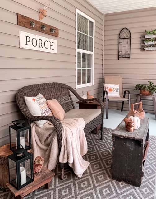 screened in back porch styled for the fall season with wicker furniture, lanterns, and cozy throw and pillows