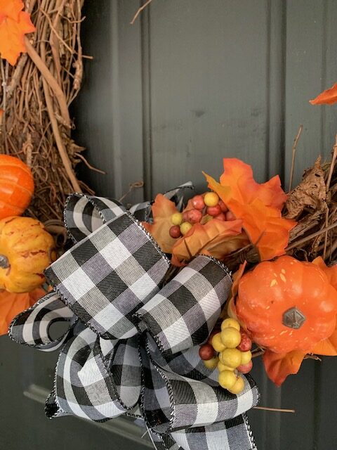 orange pumpkins and black and white buffalo check ribbon pair well for a fall wreath