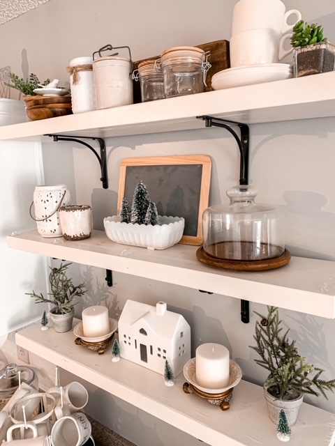 Kitchen open shelving decorated for the winter season with warm wood, glass, and winter greens