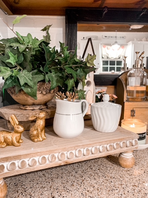 wood riser holds a spring vignette of greenery, gold bunny figurines, and coffee bar supplies
