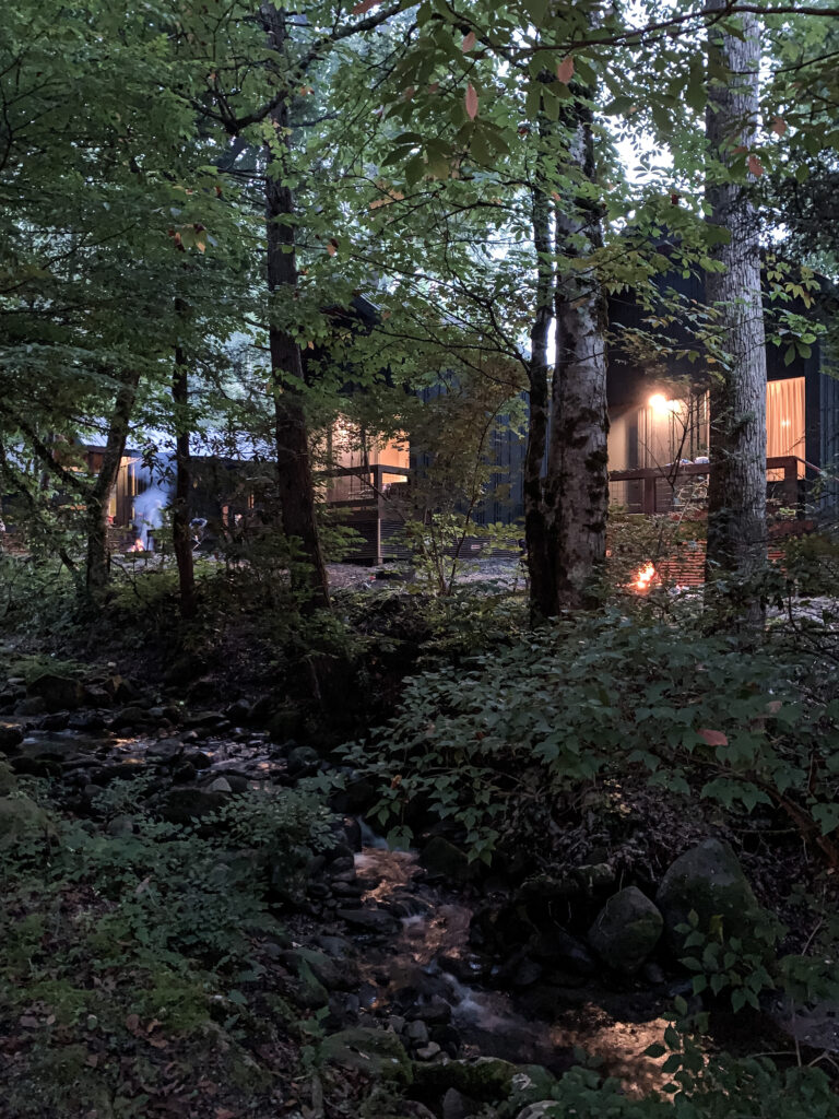 night view of a cabin next to the mountain creek with the light of the firepit